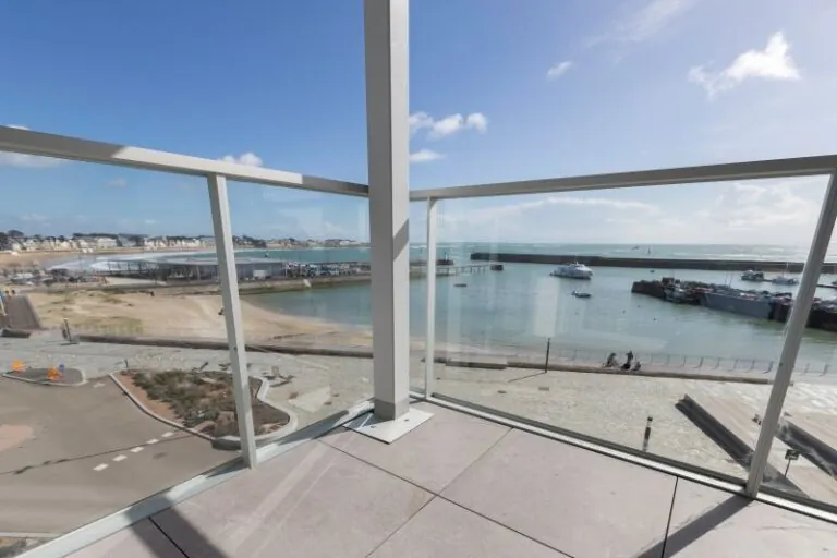 immeuble en bord de mer avec des garde-corps vitrés, vitrage clair, modèle prêt à poser avec doubles poteaux intermédiaires et habillage de la dalle avec un bandeau en aluminium